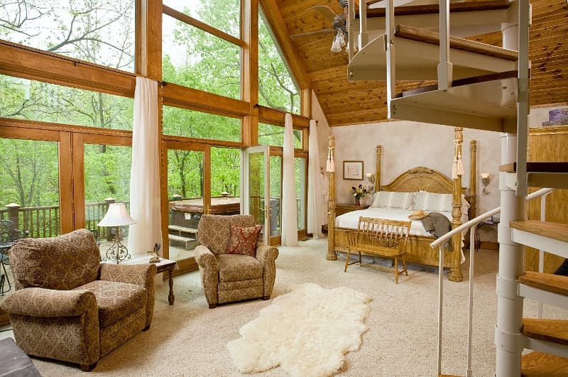 A luxurious bedroom with floor-to-ceiling windows offering stunning views, a comfortable sitting area, and a spiral staircase leading to a loft.