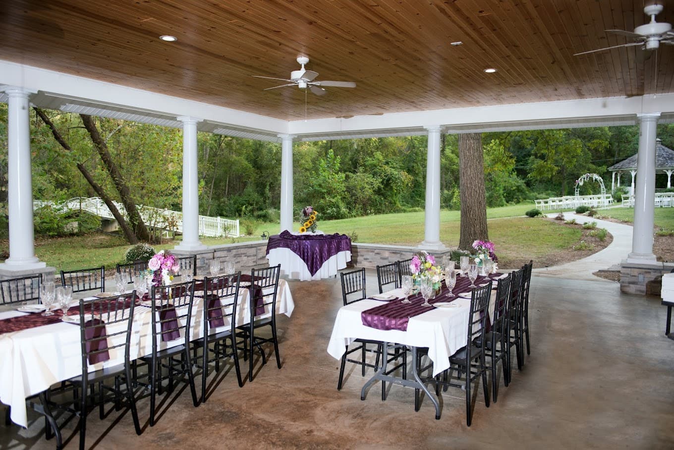 A beautifully arranged outdoor dining area with tables set for a special occasion, surrounded by greenery.