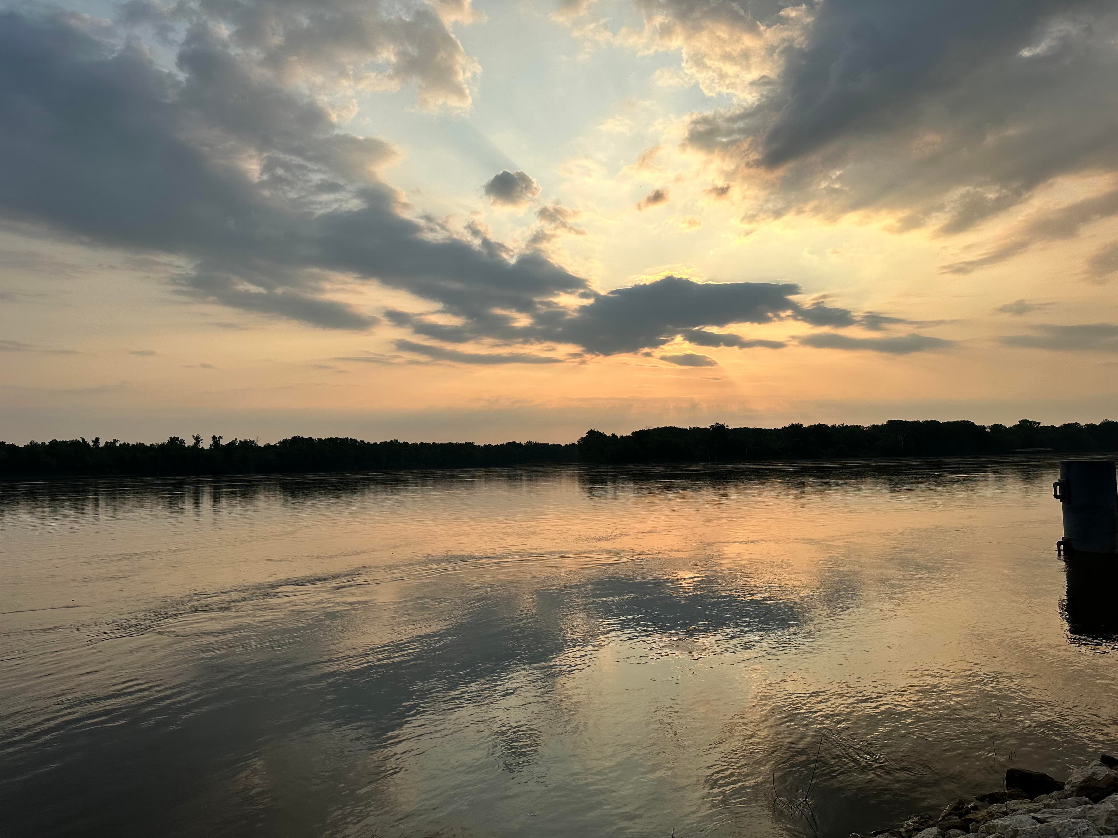 Sunset over a calm river with reflective water and cloudy skies.
