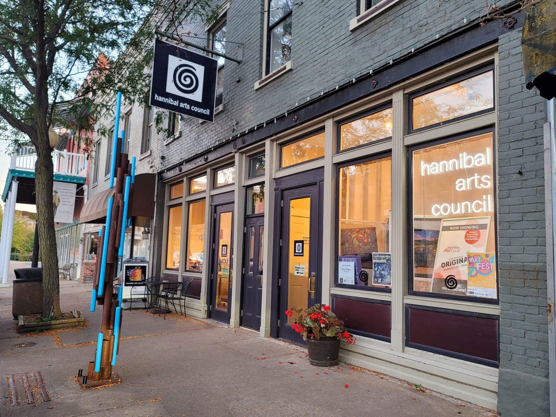 The exterior of the Hannibal Arts Council building, featuring a sign and colorful artwork displays in the windows.